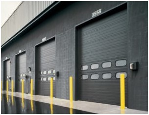 Several garage doors on a dark cinderblock commercial warehouse